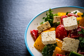Fresh Greek salad - feta cheese, tomatoes, cucumber, three color pepper, black olives and onion on black stone board
