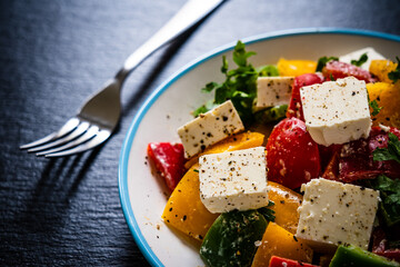 Fresh Greek salad - feta cheese, tomatoes, cucumber, three color pepper, black olives and onion on black stone board
