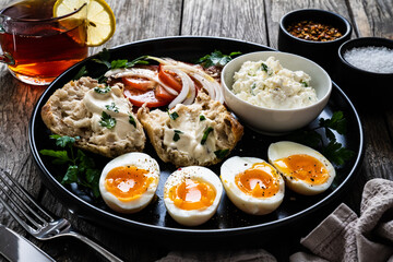 Delicious breakfast - soft boiled eggs with  cottage cheese and vegetables served on black plate on wooden table
