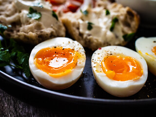 Delicious breakfast - soft boiled eggs with  cottage cheese and vegetables served on black plate on wooden table
