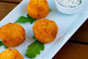 Delicious potato croquettes in a white plate on a wooden table.