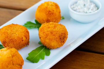 Delicious potato croquettes in a white plate on a wooden table.