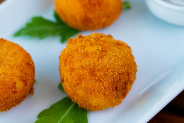 Delicious potato croquettes in a white plate on a wooden table.