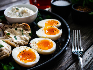 Delicious breakfast - soft boiled eggs with  cottage cheese and vegetables served on black plate on wooden table
