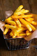 Delicious crispy french fries in a metall basket on a wooden table.