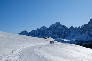 Beautiful winter view of mountains - silhouettes of walking tourists on snowy road leading to Alpe di Nemes refuge in Sexten Dolomites, South Tyrol, Italy