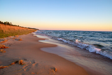 Golden sunset on a wide sandy beach along the coast of Lake Michigan as waves crash onto the shore.