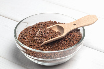 Flax seeds in the glass bowl on white wooden table. Close -up. Horizontal orientation.