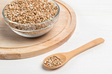 Green buckwheat in the glass bowl and in the wooden spoon on white table.