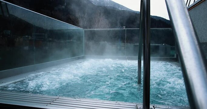 An empty outdoor jacuzzi with steam. We can see mountains in the background, perfect leisure activity in winter holidays 4K