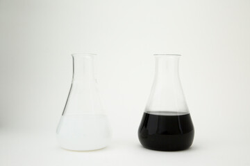 Scientific laboratory glass erlenmeyer flask filled with white and black liquid on white background.