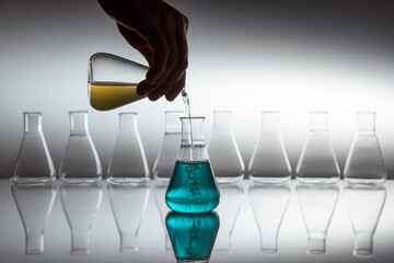 Hand pouring yellow in to blue liquid in scientific laboratory glass erlenmeyer flask with...