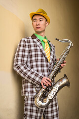 Asian guy with saxophone standing against a wall