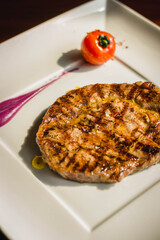 a slab of grilled beef steak served with grilled tomato and taro puree on a white plate
