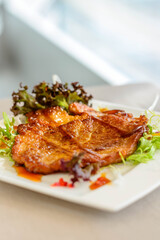 main course of Pan-fried Pork Chop with Soy Sauce served on lettuce on a white plate