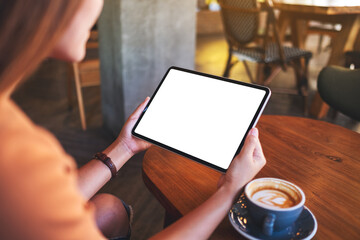 Mockup image of a woman holding digital tablet with blank white desktop screen with coffee cup on wooden table