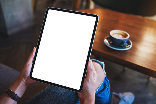 Mockup image of a woman holding digital tablet with blank white desktop screen with coffee cup on wooden table