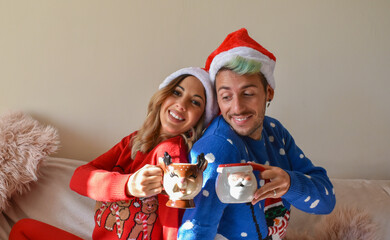Happy couple dressed in Christmas clothes, having a hot drink at home.