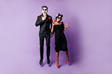 Funny young people with face art on Halloween emotionally pose, jumping on purple background