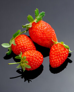 Macro image of fresh red strawberries group isolated at black background with reflection.