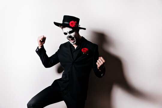 Active man in black suit reacts emotionally to winning. Snapshot of guy in image for masquerade on white background with his own shadow