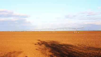 Plowed agricultural field in spring with blue sky. Agriculture and food processing, environmental protection theme. Irrigation equipment sprinklers, irrigation system.