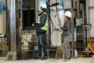 Fototapeta premium Portrait of a female factory manager in a white hard hat and business suit and factory engineer in work clothes. Controlling the work process in the manufacture.