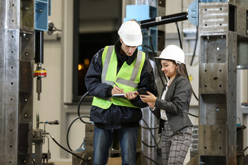 Portrait of a female factory manager in a white hard hat and business suit and factory engineer in work clothes. Controlling the work process in the manufacture.