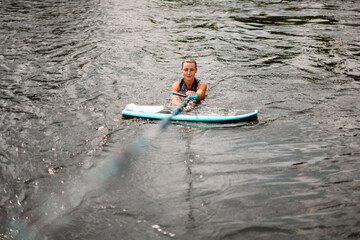 wet woman in the water holding tight rope and board for wake nearby