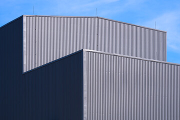 Fototapeta na wymiar Sunlight and shadow on surface of gray corrugated metal factory building against blue sky background