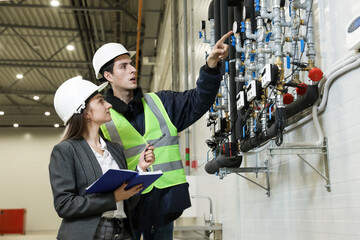 Portrait of a female factory manager in a white hard hat and business suit and factory engineer in work clothes. Controlling the work process in the manufacture.