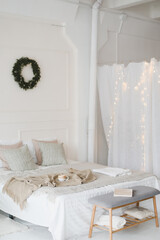 Bed with beige knitted plaid and a cup. Interior of stylish cozy bedroom with wreath on the wall. Christmas, New year  home decor