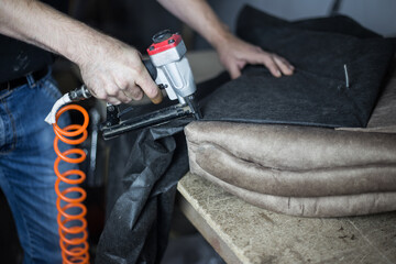Furniture making process. Young man sheathes part of the sofa with a stapler on the desktop