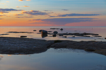 Fototapeta na wymiar Beautiful colorfull sunset over the sea shore with rocks under shallow water