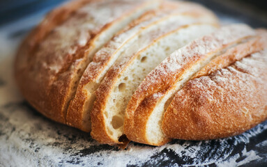 Sliced delicious wheat bread that was recently prepared and still lies on the baking tray, sprinkled with flour. Home cooking.