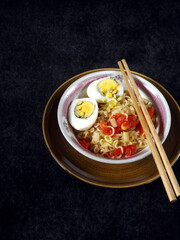 A bowl of simple noodles with chili, tomato, spring onion, and egg. Simple menu for breakfast. High angle with black background.