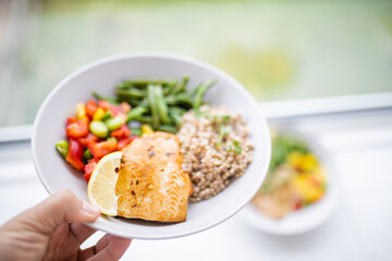 Hand holding salmon and buckwheat dish with green beans