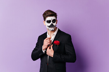Man in skull mask winks coquettishly, posing with overlaid mustache for portrait on isolated background