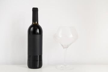 Black bottle of red wine on a white background with copy space. Wine mockup on the table with a glass