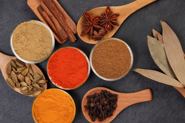 Mix variety spice cinnamon cardamom clove bay leaf wooden chilli cumin turmeric powered on black slate background