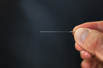 Closeup of an acupuncture needle being held between fingertips