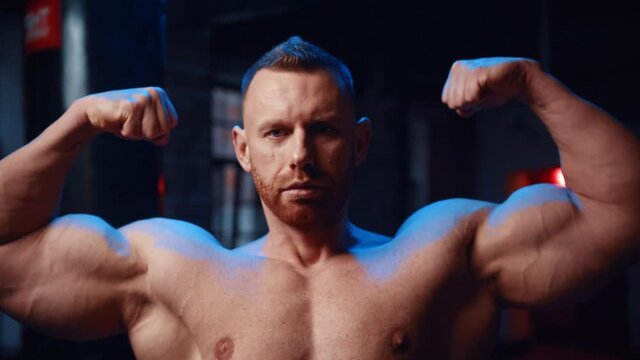 Strong man standing in the gym and showing his biceps