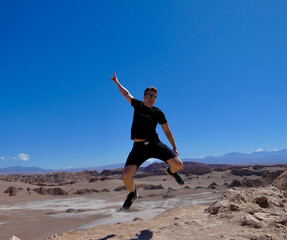 Fototapeta premium Young man with sunglasses jumping in pose, valley of the moon, Atacama, Chile