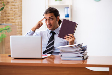 Fototapeta premium Young male student employee reading book at workplace