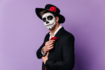 Closeup portrait of guy in Halloween costume in Mexican style, complementing outfit with red rose