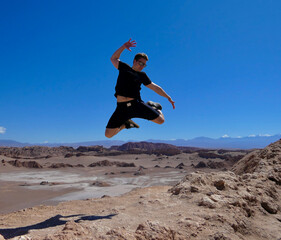 Active young man with sunglasses jumping in valley of the moon, Atacama, Chile