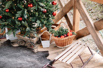 Christmas tree and sleigh on the porch of a wooden house.