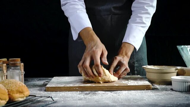 Homemade healthy food concept. Hand of baker chef man wear black apron kneading dough for making bread on the wooden board. 