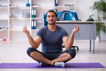 Fototapeta premium Young handsome employee doing sport exercises in the office
