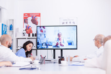 Group of doctors discussing with expert during video conference from hospital meeting room....